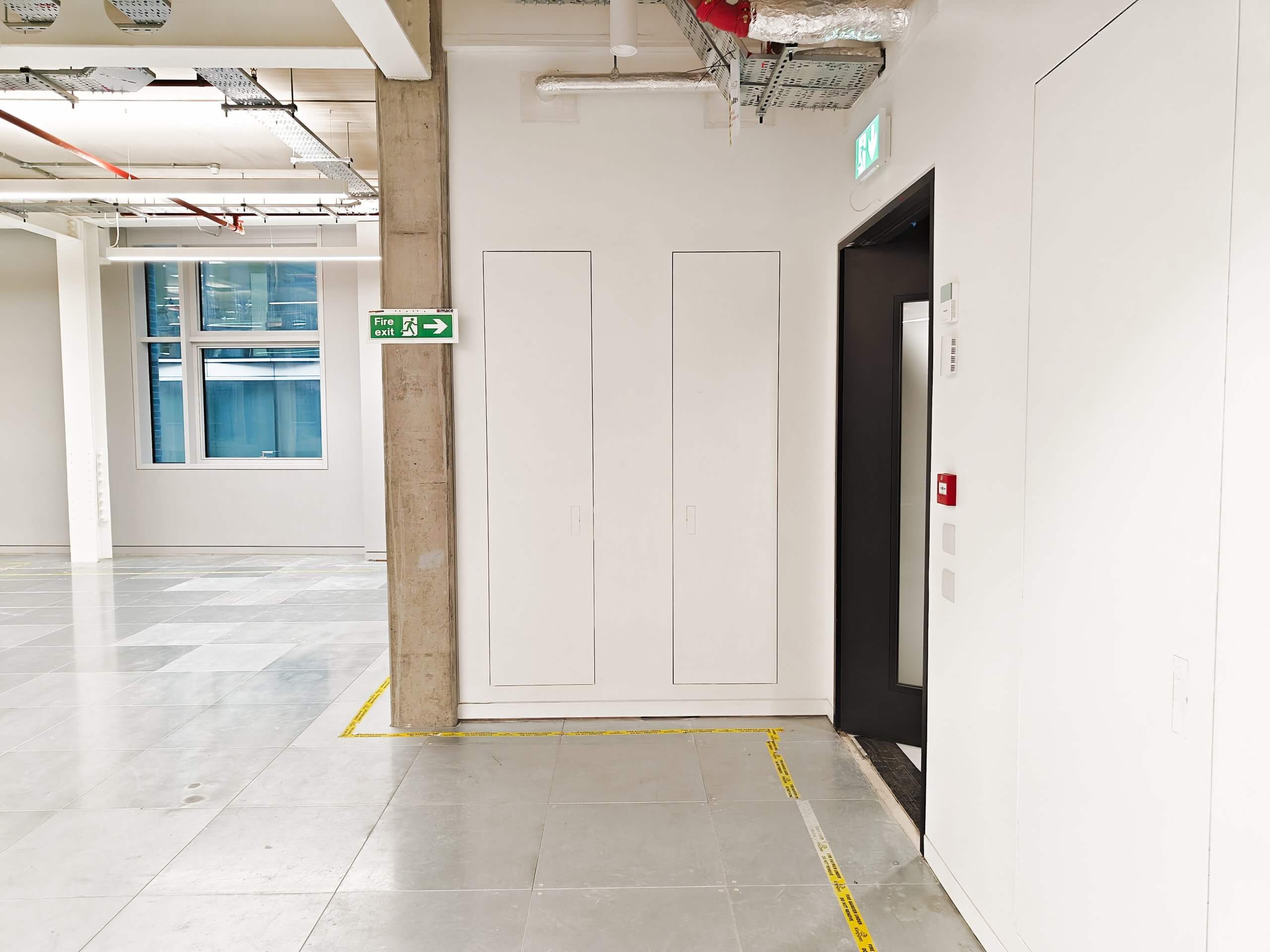 Construction worker in a high-visibility vest and hard hat inspecting an open Christo Riser Door in a modern commercial space. Additional closed Christo Riser Doors and exposed ceiling infrastructure are visible in the background.
